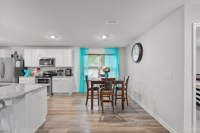 kitchen with hardwood / wood-style floors, light stone counters, stainless steel appliances, and white cabinetry