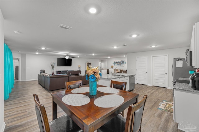 dining room with a textured ceiling, ceiling fan, light hardwood / wood-style flooring, and sink