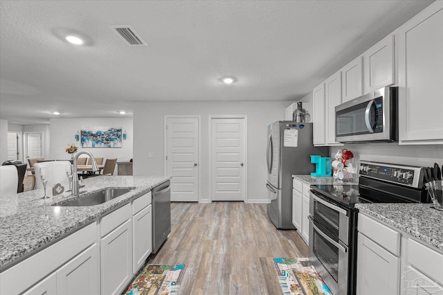 kitchen with sink, stainless steel appliances, a textured ceiling, white cabinets, and light stone counters