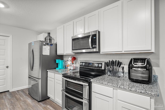 kitchen featuring light wood-type flooring, appliances with stainless steel finishes, a textured ceiling, white cabinets, and light stone counters