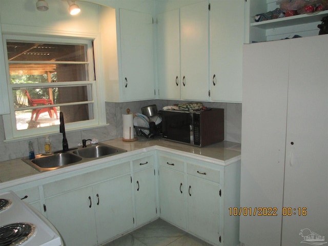 kitchen with tasteful backsplash, white cabinetry, range, and sink