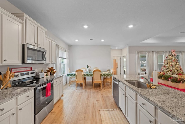 kitchen with sink, white cabinetry, light stone counters, light hardwood / wood-style flooring, and appliances with stainless steel finishes