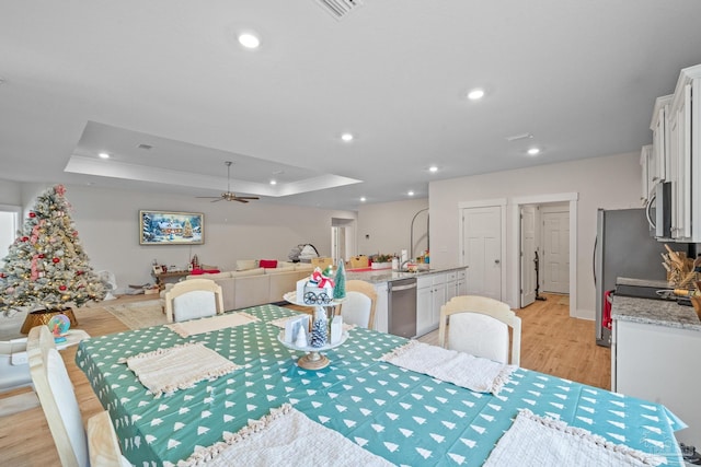 dining space with sink, a raised ceiling, ceiling fan, and light wood-type flooring