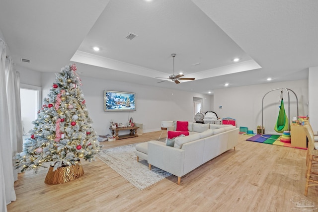 living room with ceiling fan, a tray ceiling, ornamental molding, and light hardwood / wood-style flooring