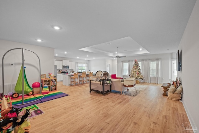 recreation room featuring light hardwood / wood-style floors, ceiling fan, and a raised ceiling