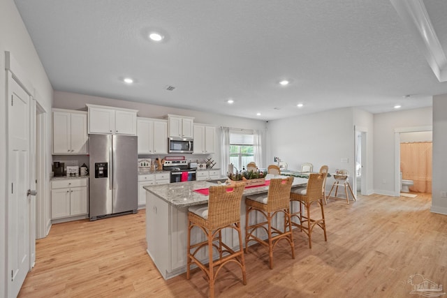 kitchen with appliances with stainless steel finishes, white cabinetry, a kitchen island with sink, and a breakfast bar area