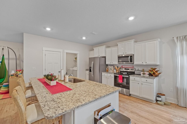 kitchen with appliances with stainless steel finishes, a breakfast bar, an island with sink, and white cabinetry