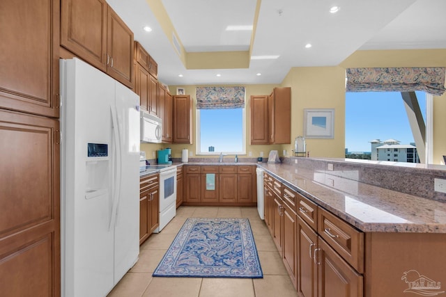 kitchen with kitchen peninsula, a tray ceiling, light stone countertops, light tile patterned floors, and white appliances