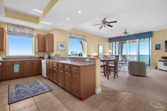 kitchen featuring kitchen peninsula, light stone counters, ceiling fan, sink, and light colored carpet