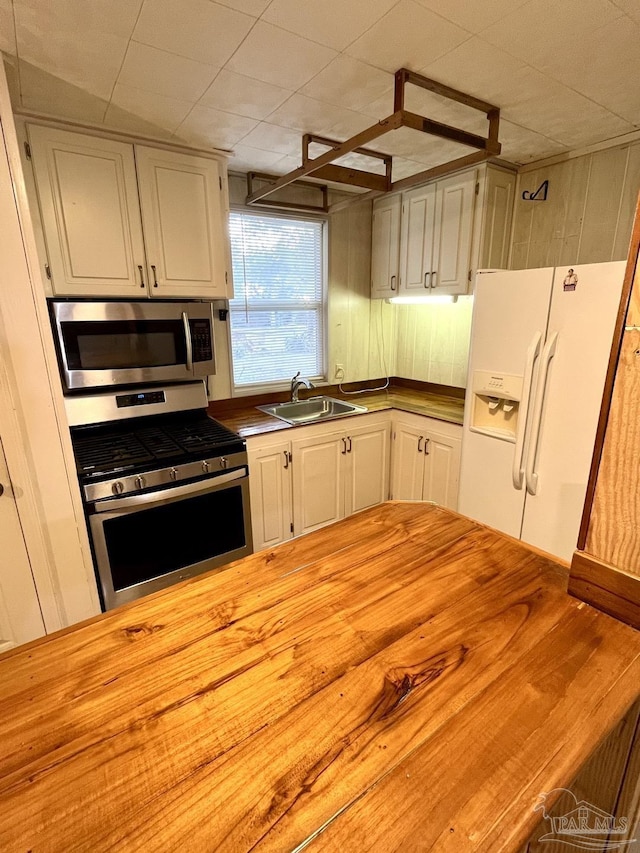 kitchen featuring butcher block countertops, appliances with stainless steel finishes, white cabinets, and a sink