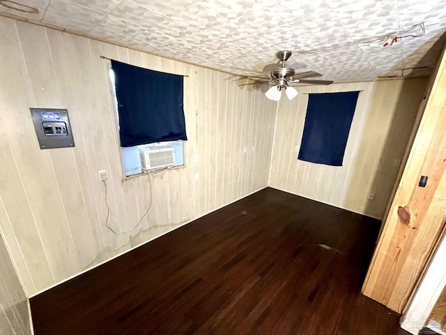 empty room with a ceiling fan, cooling unit, wooden walls, and wood finished floors