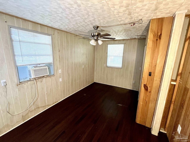 empty room featuring cooling unit, ceiling fan, wooden walls, and wood finished floors