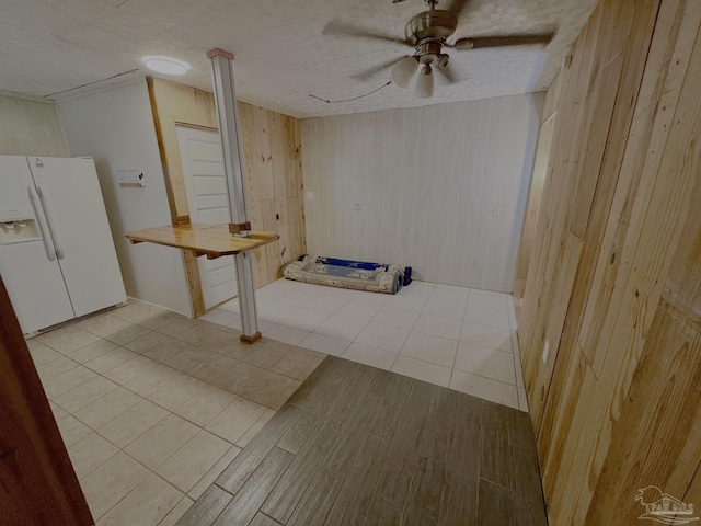 interior space featuring white refrigerator with ice dispenser, wood walls, wood finished floors, and a ceiling fan