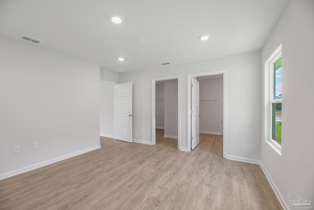 unfurnished bedroom featuring light hardwood / wood-style floors, a spacious closet, a closet, and multiple windows