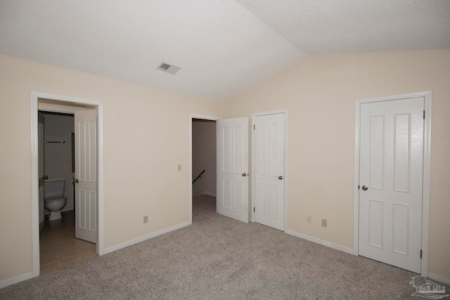 unfurnished bedroom with connected bathroom, lofted ceiling, a textured ceiling, and light colored carpet