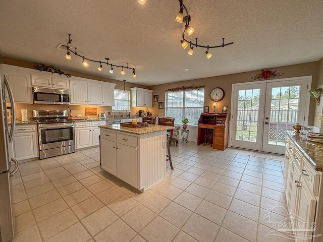 5020 Lantana Dr, Gulf Breeze, FL 32563 - kitchen featuring appliances with stainless steel finishes, light tile patterned flooring, white cabinetry, a kitchen island, and french doors