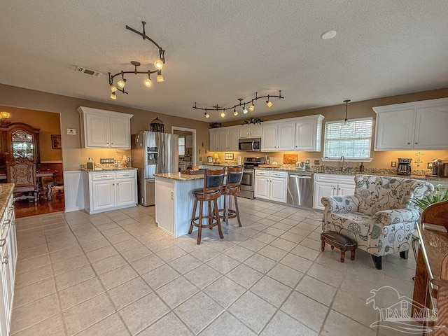 5020 Lantana Dr, Gulf Breeze, FL 32563 - kitchen with stainless steel appliances, light tile patterned floors, white cabinetry, a textured ceiling, and a kitchen breakfast bar