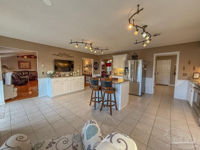 5020 Lantana Dr, Gulf Breeze, FL 32563 - kitchen with stainless steel fridge, light tile patterned flooring, white cabinets, a wainscoted wall, and a textured ceiling
