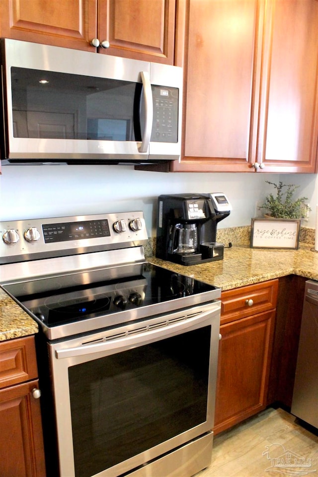 kitchen with stainless steel appliances, light stone counters, and light hardwood / wood-style flooring