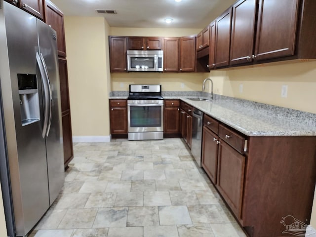 kitchen featuring light stone counters, stainless steel appliances, sink, and dark brown cabinets