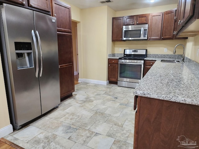 kitchen with light stone countertops, stainless steel appliances, sink, and dark brown cabinetry