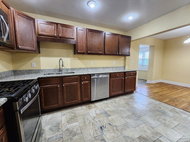 kitchen featuring appliances with stainless steel finishes, sink, light stone counters, dark brown cabinetry, and light wood-type flooring