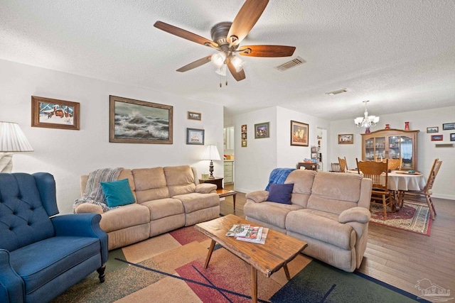 living room with a textured ceiling, wood-type flooring, and ceiling fan with notable chandelier