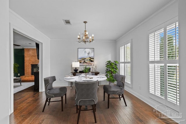 dining area with dark hardwood / wood-style flooring, ornamental molding, a brick fireplace, and an inviting chandelier