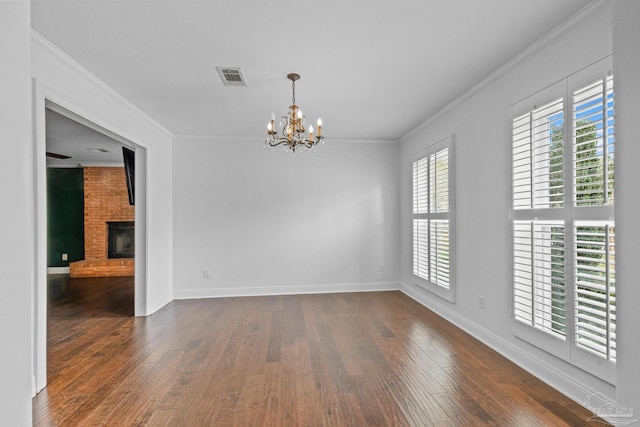 empty room with ornamental molding, dark hardwood / wood-style flooring, a chandelier, and a brick fireplace