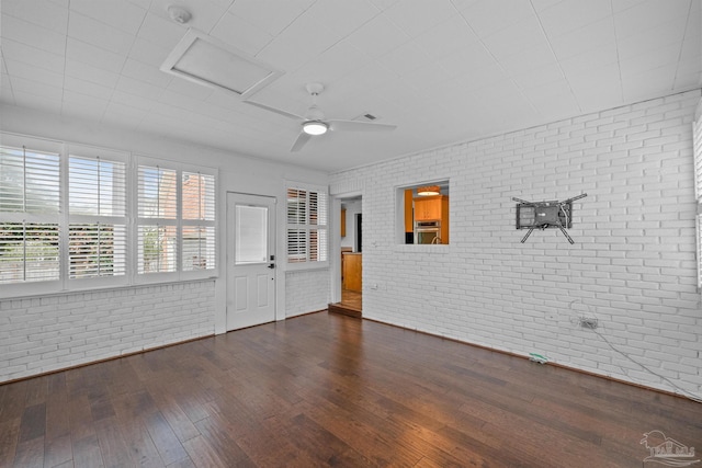 spare room with dark wood-type flooring, ceiling fan, and brick wall