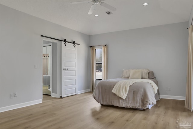 bedroom featuring ceiling fan, a barn door, and light wood-type flooring