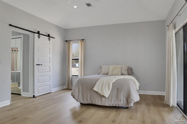 bedroom with a barn door and light wood-type flooring