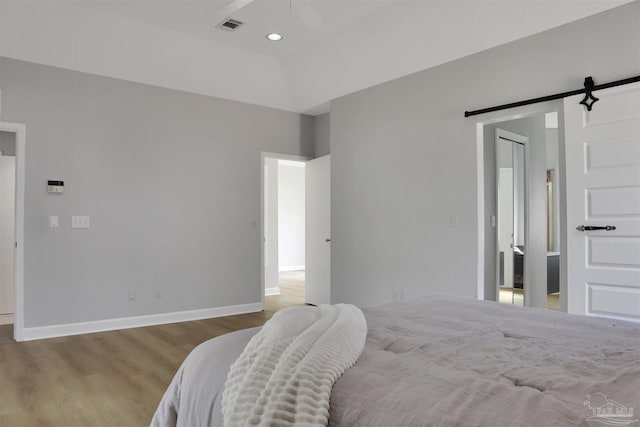 bedroom with a barn door, vaulted ceiling, and light wood-type flooring