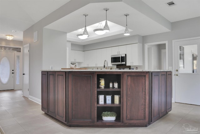 kitchen with dark brown cabinetry, light tile patterned floors, decorative light fixtures, and a tray ceiling