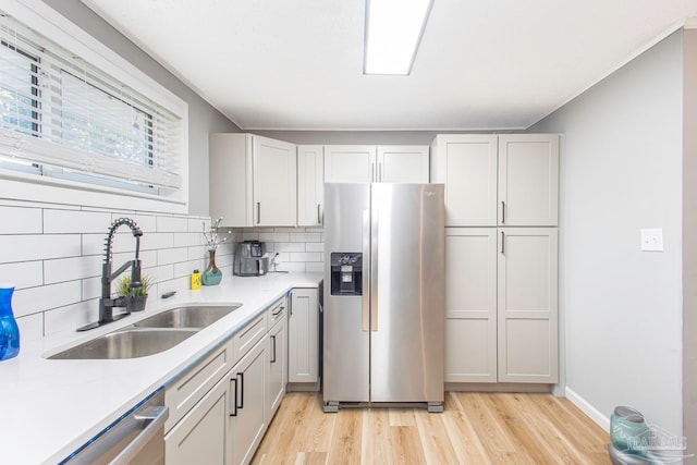 kitchen featuring white cabinetry, sink, stainless steel appliances, tasteful backsplash, and light hardwood / wood-style floors