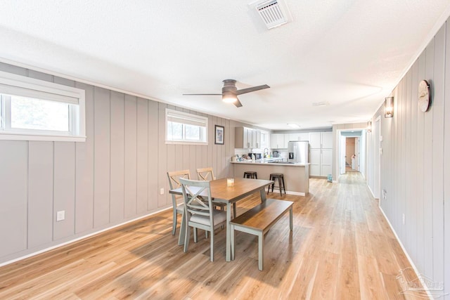 dining area with wood walls, light hardwood / wood-style flooring, ceiling fan, and a textured ceiling