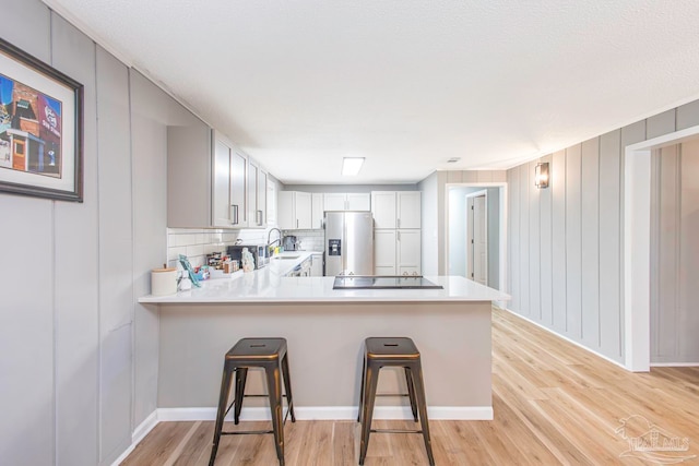 kitchen featuring a breakfast bar, backsplash, stainless steel refrigerator with ice dispenser, light wood-type flooring, and kitchen peninsula