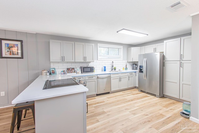 kitchen with kitchen peninsula, appliances with stainless steel finishes, light wood-type flooring, sink, and a breakfast bar area