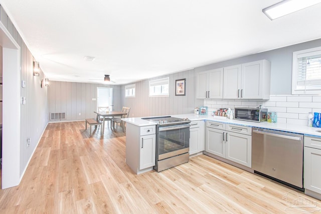 kitchen with kitchen peninsula, appliances with stainless steel finishes, light wood-type flooring, and tasteful backsplash