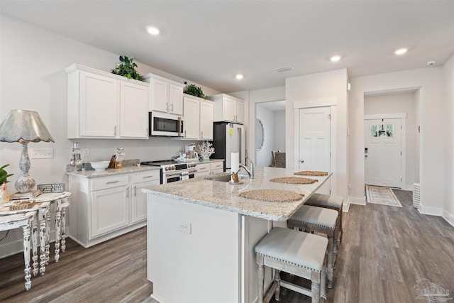 kitchen with light stone countertops, stainless steel appliances, sink, white cabinetry, and an island with sink