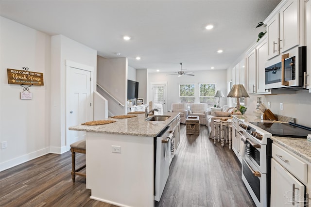 kitchen with stainless steel appliances, sink, white cabinets, dark hardwood / wood-style floors, and an island with sink