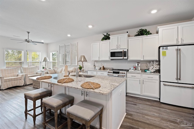 kitchen featuring dark wood-type flooring, a center island with sink, sink, premium appliances, and white cabinetry