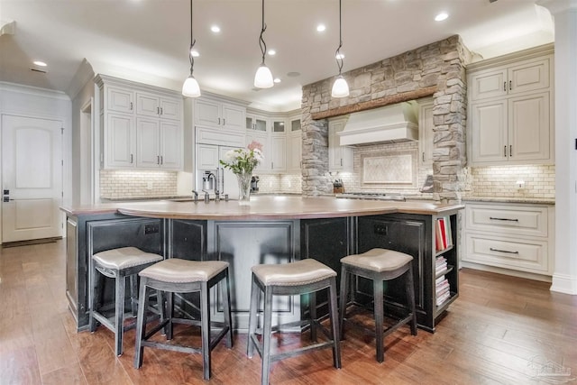 kitchen with hardwood / wood-style floors, a kitchen bar, custom range hood, hanging light fixtures, and a kitchen island with sink