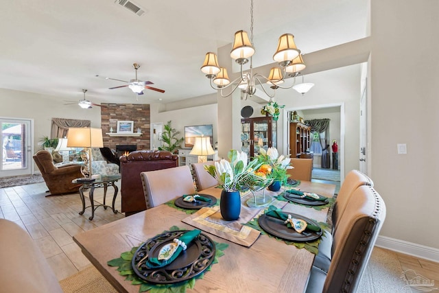 dining area featuring ceiling fan with notable chandelier, light hardwood / wood-style flooring, brick wall, and a large fireplace