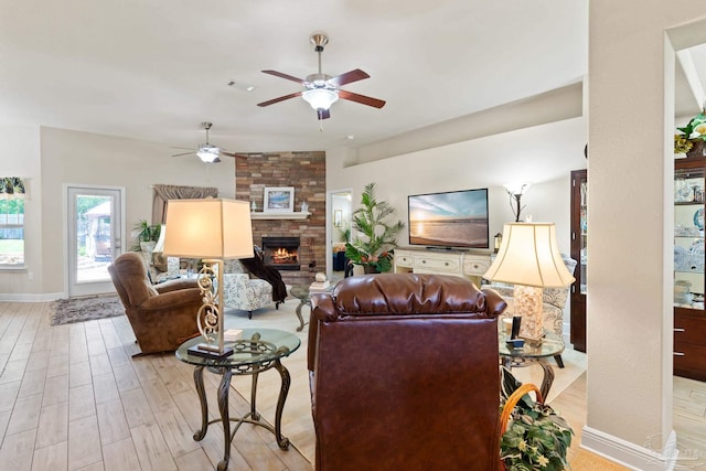 living room with brick wall, light wood-type flooring, ceiling fan, and a large fireplace