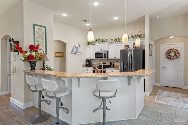 kitchen featuring a breakfast bar, light wood-type flooring, kitchen peninsula, white cabinets, and appliances with stainless steel finishes