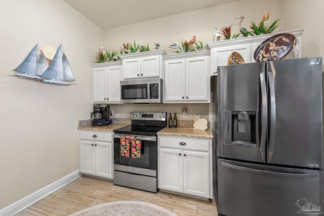 kitchen featuring white cabinetry, light stone countertops, appliances with stainless steel finishes, and light wood-type flooring