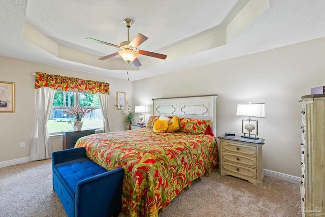 bedroom with a textured ceiling, ceiling fan, a raised ceiling, and light colored carpet