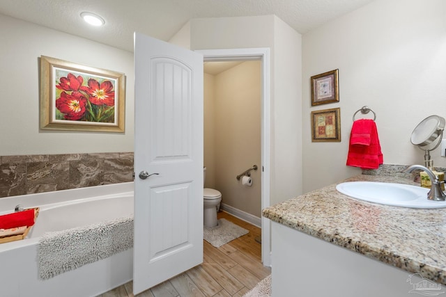 bathroom with a bath, a textured ceiling, toilet, vanity, and wood-type flooring