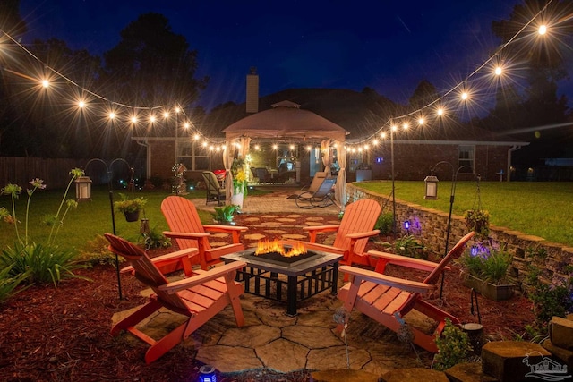 patio at twilight with a fire pit, a yard, and a gazebo